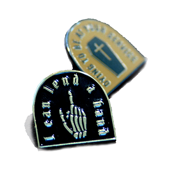 enamel pin of
  a skeleton hand pointing upwards and text that reads 'i can lend a hand'
  colored black and set in gold metal